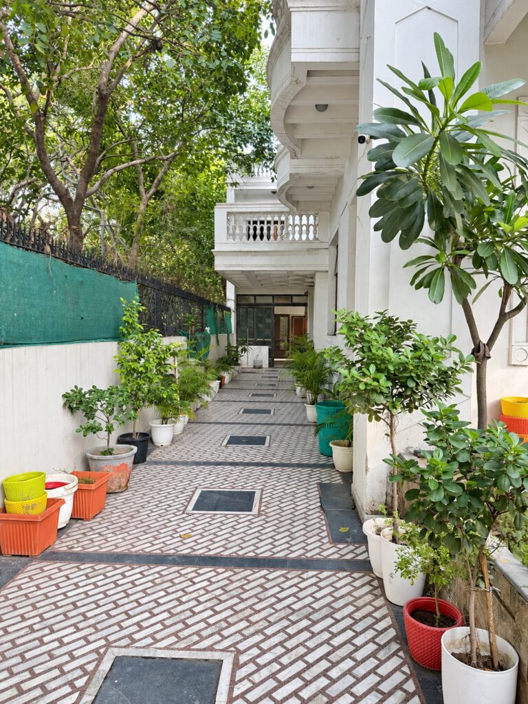 Plant-lined tiled entrance walkway at GableStay girls’ PG in Sector 33, Noida