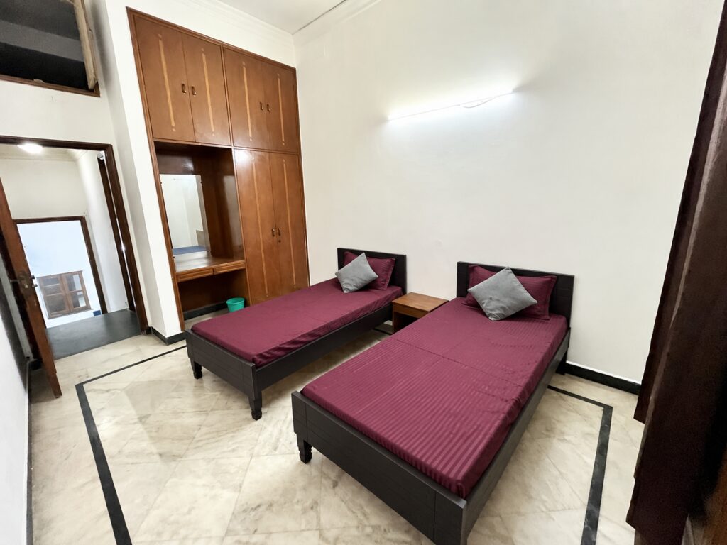 Furnished double-sharing room with two wooden beds and built-in wardrobe at GableStay IVA girls’ PG, Sector 33, Noida